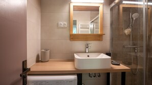 A modern bathroom with a white sink, a mirror above it, and a glass-enclosed shower. - Bright and spacious apartment close to city center (Châtel)