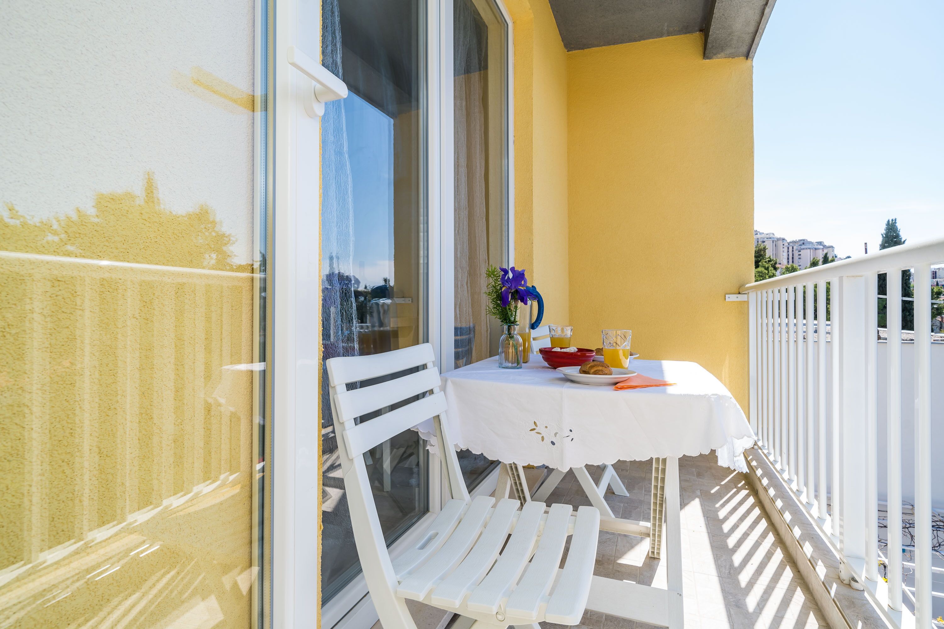 A balcony with a white table and chairs, a vase with flowers, and a plate of food.