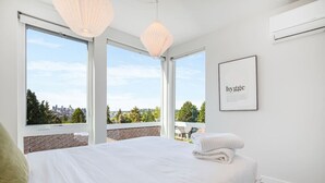 Een moderne hotelkamer met een groot bed, uitzicht op de stad en een ingelijste tekst aan de muur.