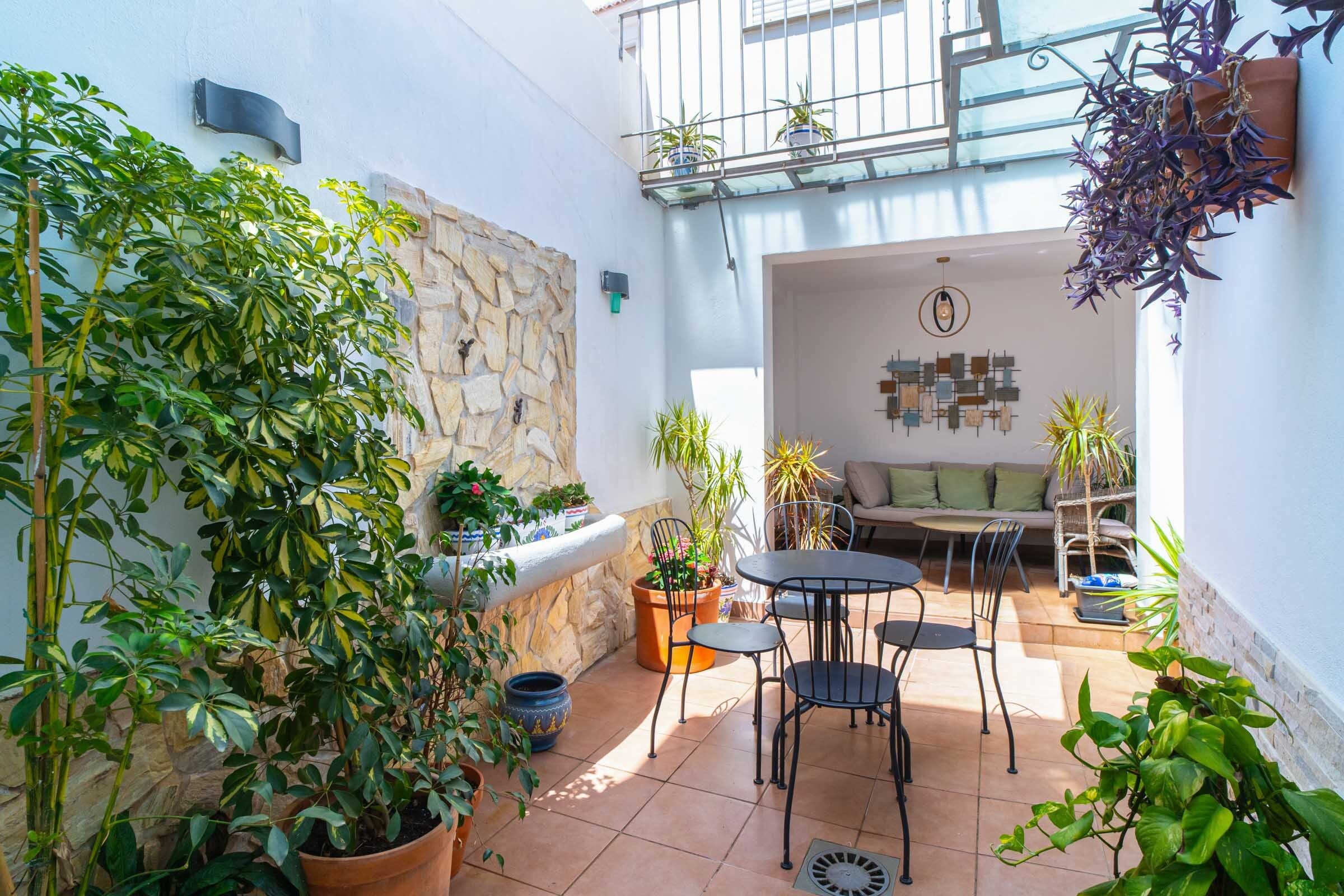 Une terrasse ensoleillée avec un mur en pierre, des plantes en pot, un coin salon avec un canapé et des fauteuils, et un élément décoratif mural.