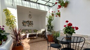 Eine sonnendurchflutete Terrasse mit Esstisch, Stühlen, Kübelpflanzen und einer Couch.