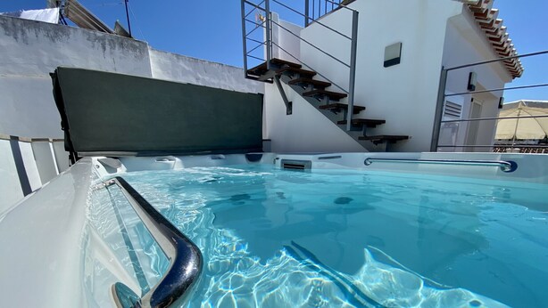 Ein Schwimmbecken mit Metallhandlauf, einer Treppe und einem weißen Gebäude im Hintergrund.