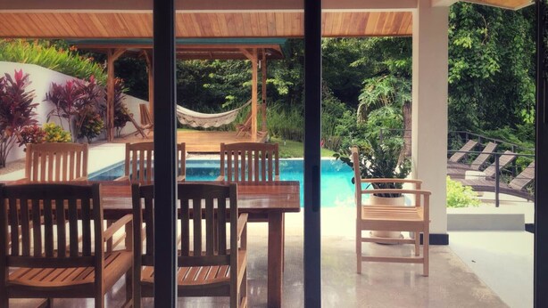 A patio with wooden furniture and a view of a swimming pool.