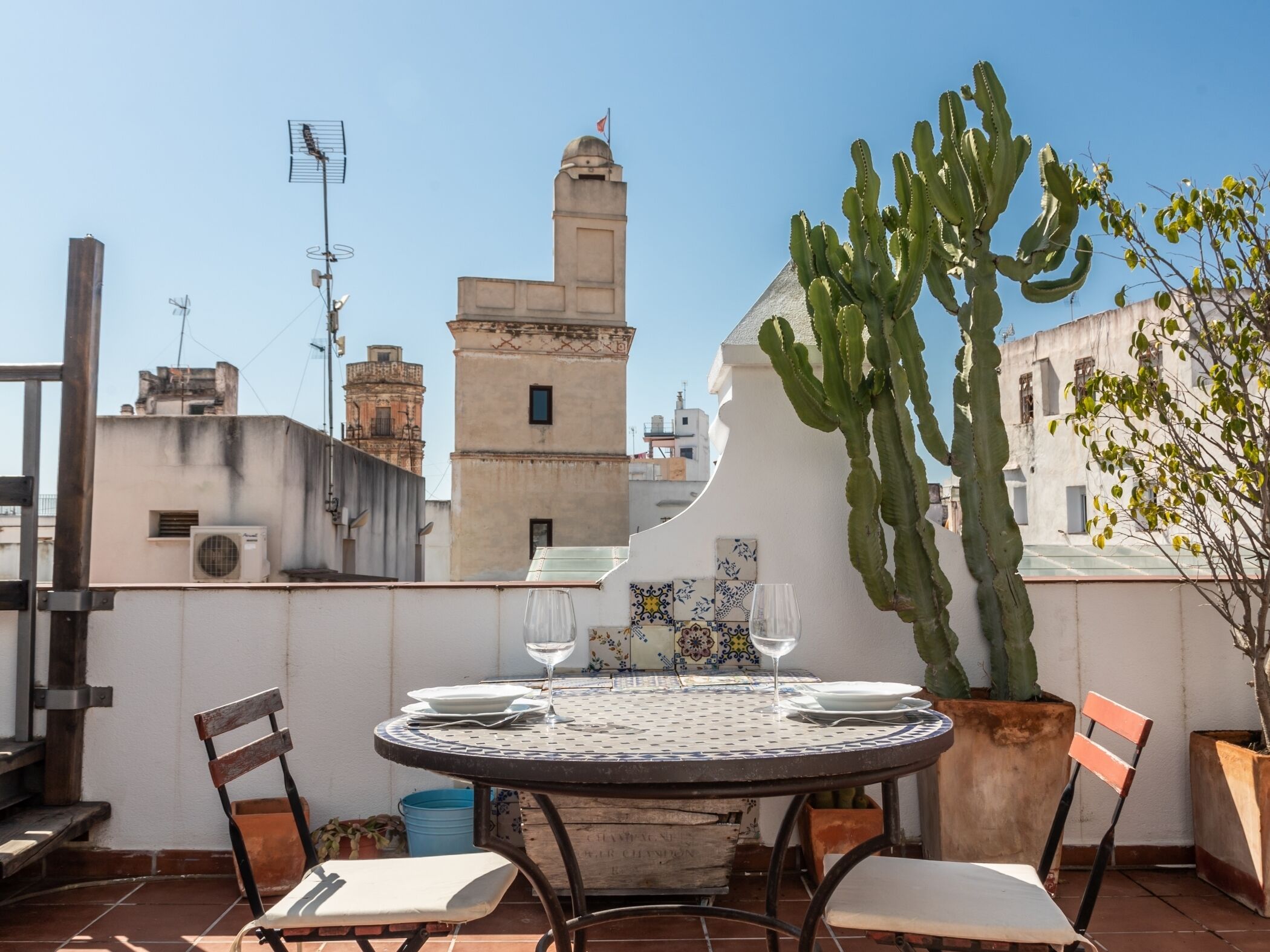 Terraza en la azotea con una mesa para dos, un cactus y vistas a edificios históricos.