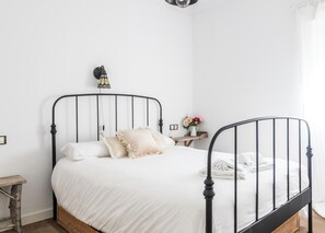 A bed with a metal frame, white bedding, and a bedside table with a vase of flowers.