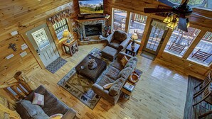 Ein gemütliches Blockhaus-Interieur mit Kamin aus Stein, Holzmöbeln und großen Fenstern mit Blick ins Freie.