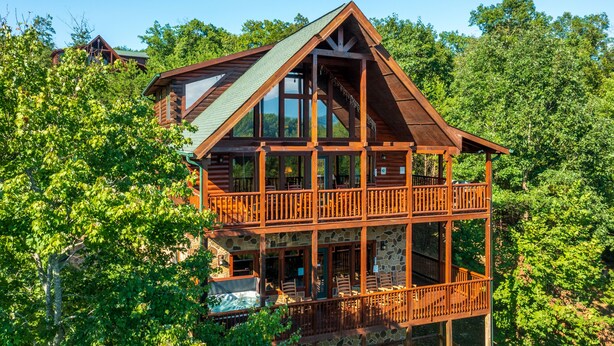 Eine zweistöckige Blockhütte mit Balkon und Steinuntergrund, umgeben von dichtem Wald.