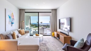 Un salon moderne comprenant un canapé, un fauteuil et un téléviseur, une table basse et une vue sur l’océan grâce à de grandes portes vitrées.