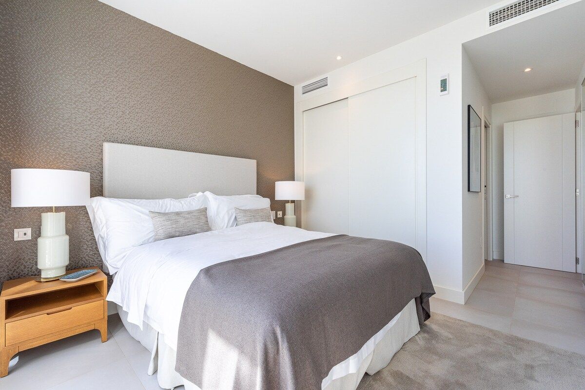A modern hotel room with a large bed, bedside lamps, a nightstand, and a wardrobe.