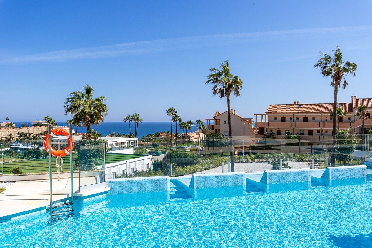 Une piscine équipée d’une bouée de sauvetage, bordée de palmiers et offrant une vue sur la mer.