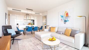 Un salon moderne avec un canapé blanc, une table basse sur laquelle on a disposé des fruits, et un coin repas avec des chaises bleues.