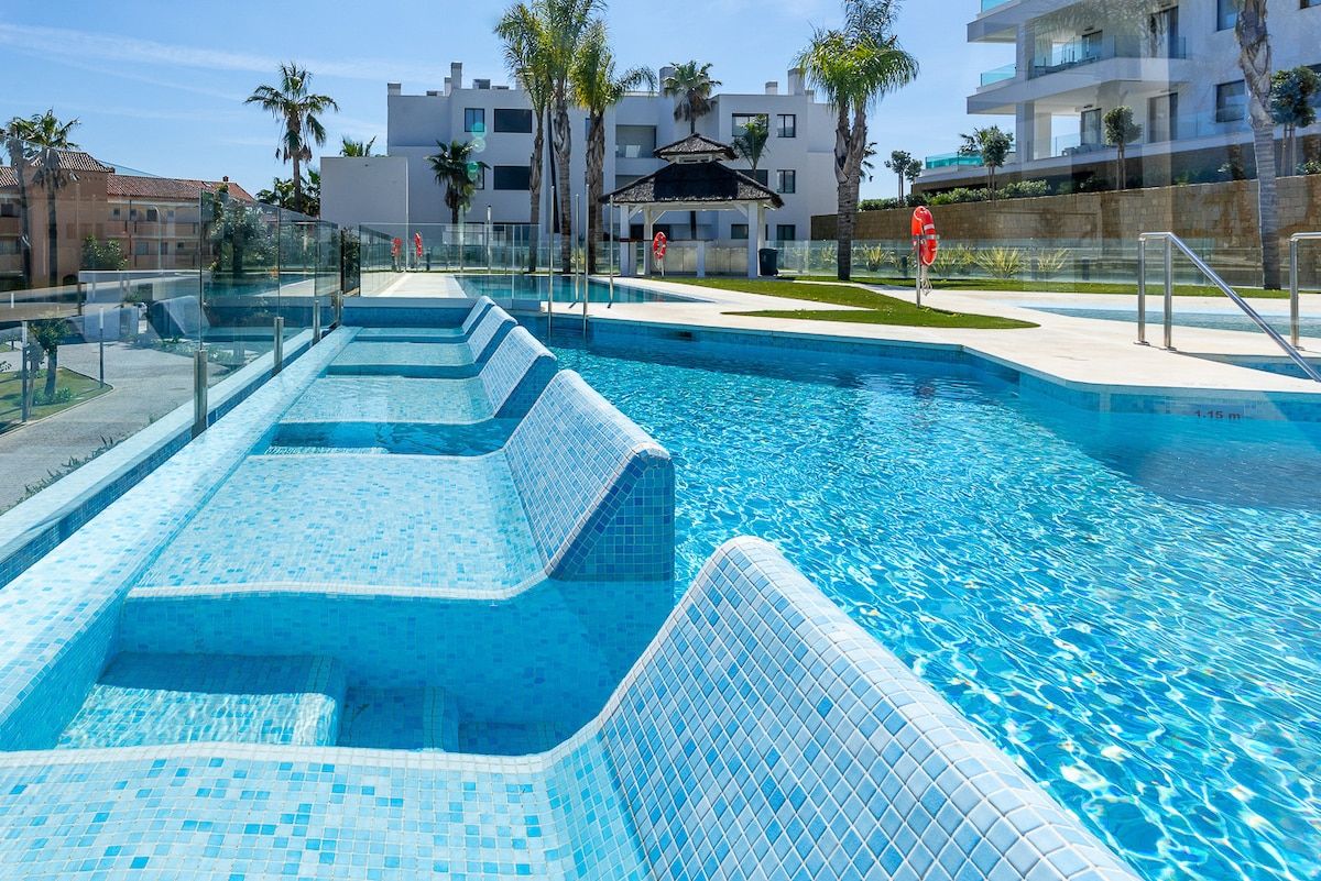 Una piscina con agua azul cristalina, rodeada por una baranda de vidrio y un pabellón al fondo.