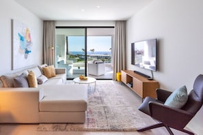 Una sala moderna con sofá, sillón, televisor de pantalla plana, una mesa de centro y vistas al exterior.