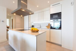 A modern kitchen with white cabinetry, a central island with a bowl of fruit, and built-in appliances.