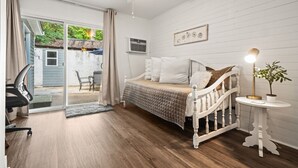 Une chambre à coucher comprenant un lit, un bureau, une chaise, un ventilateur de plafond et une vue sur l’extérieur.