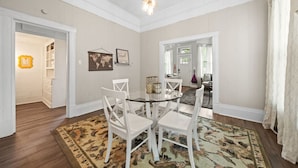 A dining area with a round glass table, white chairs, and a patterned rug. There are framed pictures on the wall and a world map. - Pet friendly 5 minute walk to Bath House! (Hot Springs)