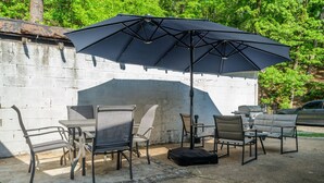An outdoor patio with a concrete wall, metal chairs, a table, and a large black umbrella. - Pet friendly 5 minute walk to Bath House! (Hot Springs)