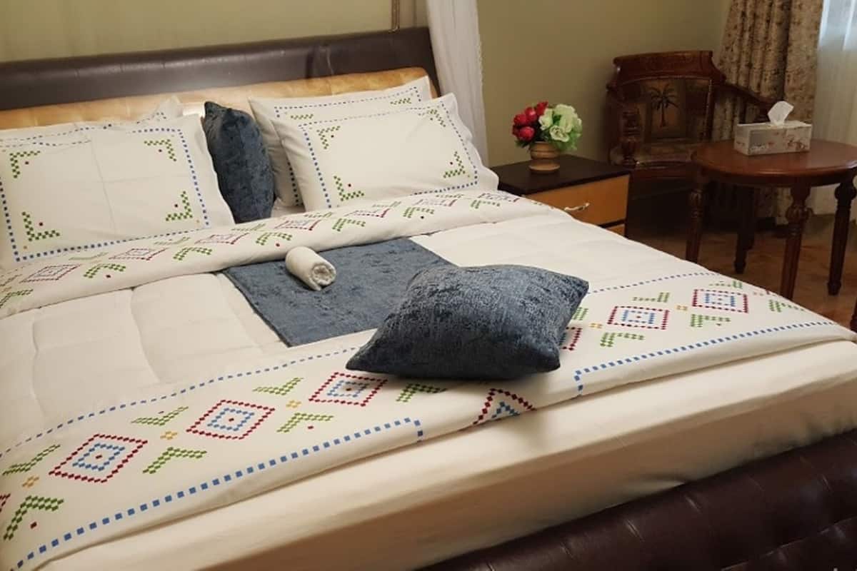A neatly made bed with a patterned bedspread, pillows, and a rolled towel.