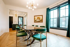 Conference room with a round table and six chairs, featuring a large window, chandelier, and framed artwork.