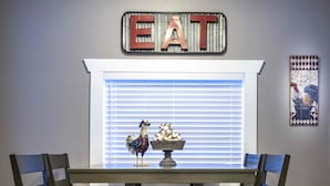 Una mesa de comedor con cuatro sillas, un gallo decorativo y un cuenco de maíz sobre la mesa.