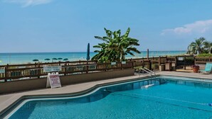 A pool area with a view of the beach, a sign indicating no infants without swim diapers, and a designated parking area.