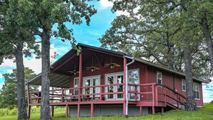 A red wooden cabin with a porch, surrounded by trees.