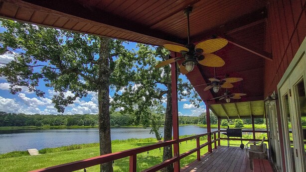 A covered deck with a view of a lake and trees.