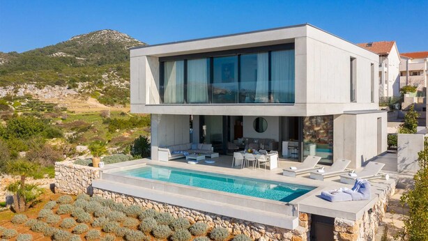 A modern two-story house with a swimming pool, outdoor seating, and a view of the surrounding landscape.
