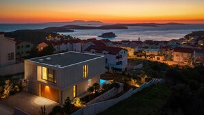 A modern building with a flat roof, a swimming pool, and a view of the sea at sunset.