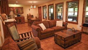 A spacious living room with a brown leather sofa, a wooden coffee table, and a dining area with wooden furniture.