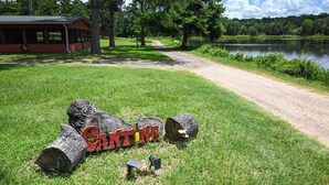 A rustic cabin with a porch, a dirt path leading to a lake, and a log with 'CANTINA' written on it.