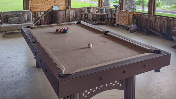 A pool table with a dartboard and billiard balls, a sofa, and a view of a lake through large windows.