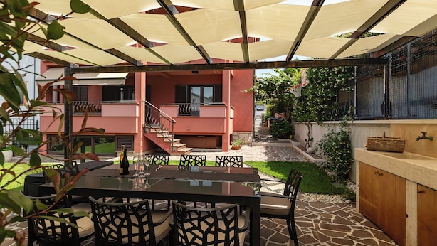 Een terras buiten met een tafel, stoelen, een barbecue en een overdekte zithoek.