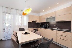 Une cuisine moderne avec un coin repas, caractérisée par des finitions en bois clair, des appareils en acier inoxydable et un luminaire suspendu.