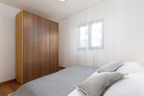 A bedroom with a bed, a wardrobe, and a window with sheer curtains.