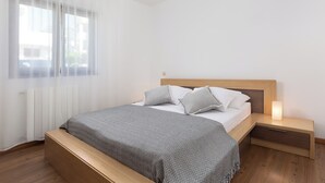 A bedroom with a bed, bedside tables, a nightstand, a bench, a window with sheer curtains, and a radiator. - Apartment Mares Family 5+ 100m2 with parking and garden (Porec)