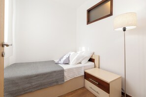 Une petite chambre à coucher avec un lit, une table de chevet, une lampe et une porte.