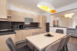 A modern kitchen with a dining area, featuring light wood cabinets, a microwave, and a dining table with chairs.
