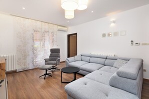 Un salon moderne avec un canapé d’angle, une table basse ronde, un fauteuil gris et une cloison en verre ornée d’un motif floral.