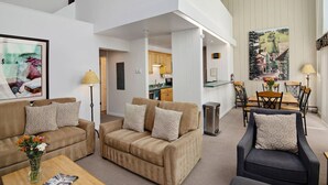 A spacious living area with a sofa set, a coffee table, and a dining table with chairs. There is a kitchen visible in the background.