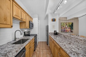 Una cocina con armarios de madera, encimera de granito, pileta de acero inoxidable, microondas, refrigerador y un cuadro en la pared.