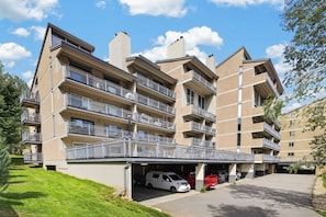 A multi-story residential building with balconies, a covered parking area, and a grassy lawn.