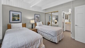 Et hotelværelse med to senge, et natbord med lampe, et spejl og en dør til et badeværelse.