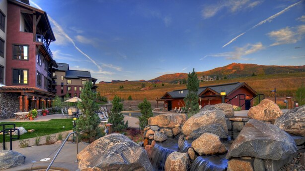 A hotel with a pool area, large rocks, and a view of the surrounding mountains. - Gorgeous & Spacious Condo W/shared Pool, Three hot Tubs, Fitness & Game Room (Steamboat Springs)