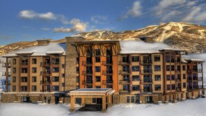 Ett hotell med flera våningar, balkonger, en fasad av sten och ett snötäckt berg i bakgrunden.