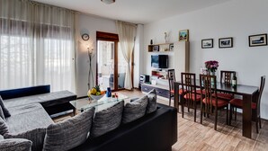 A modern living room with a sofa, dining table, chairs, and a TV. - 3BR Villa w Amazing Hilltop View on Budva Riviera (Lapčići)