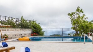 A pool area with lounge chairs, a floating pool toy, and a stone wall. - 3BR Villa w Amazing Hilltop View on Budva Riviera (Lapčići)