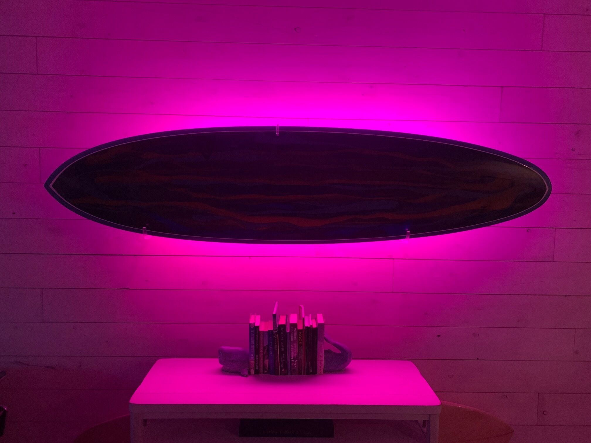 Una habitación con una mesa blanca y un espejo ovalado iluminado con luz rosa.