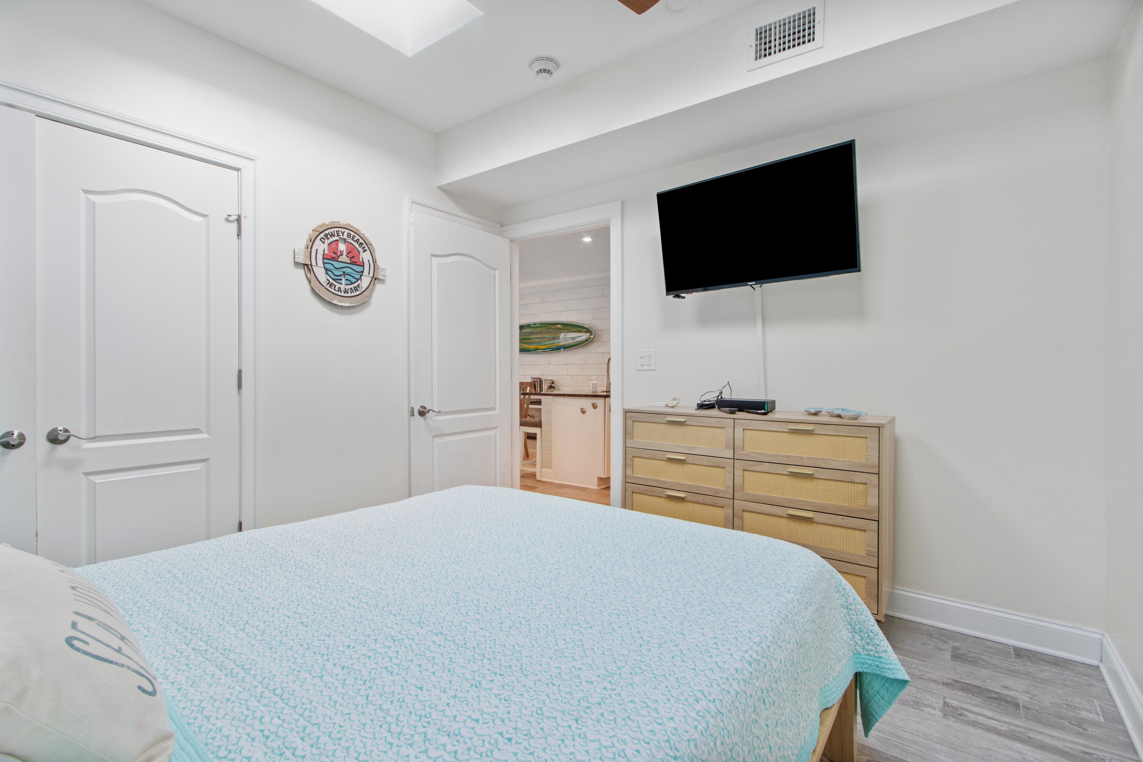 Une chambre à coucher avec un lit, une commode, un téléviseur et une porte.