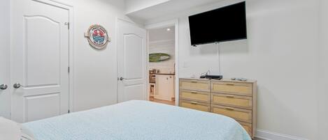 Une chambre à coucher avec un lit, une commode, un téléviseur et une porte.